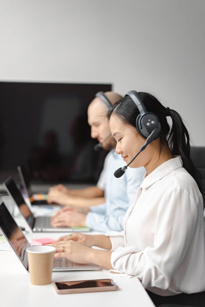 A diverse group of call center agents wearing headsets and working on laptops indoors.